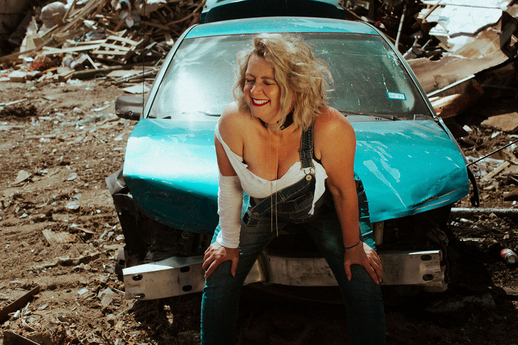 D. LeD leaning against a turquoise car in a demolition yard